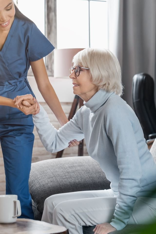 caregiver-supporting-senior-in-their-home Caregiver helping senior get up from chair in home